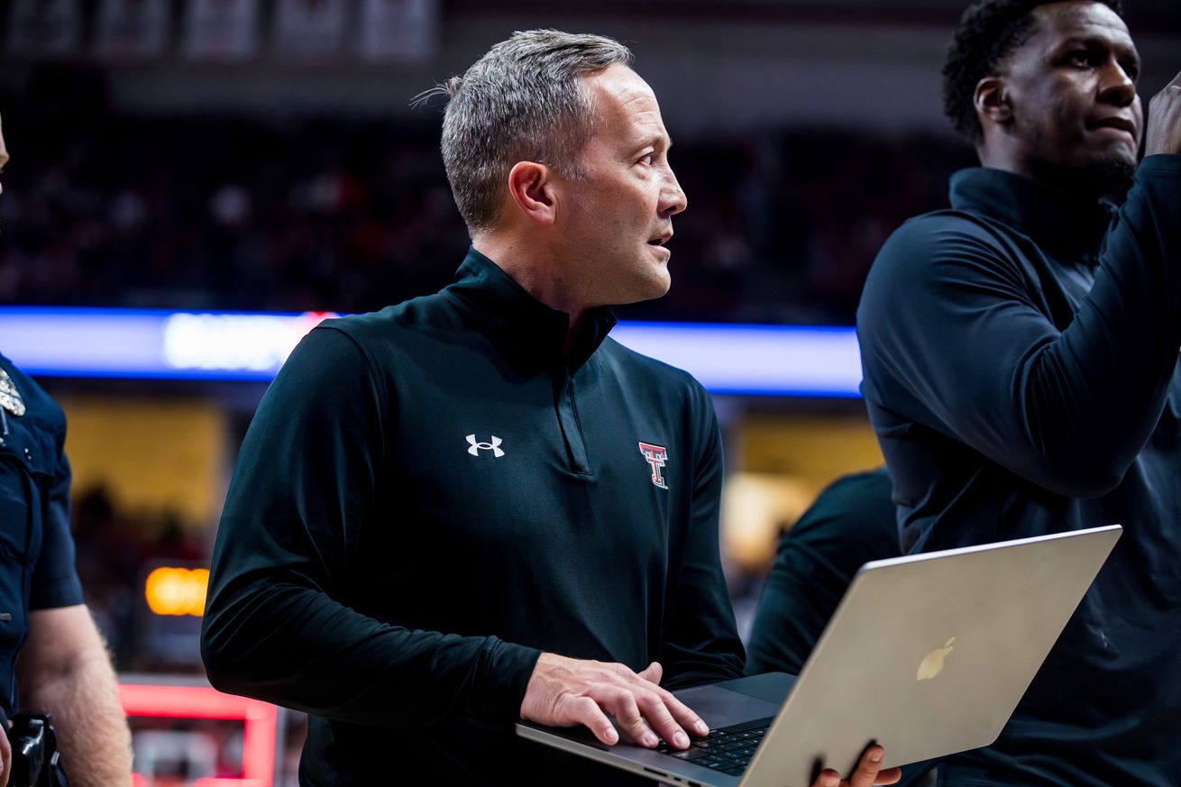 A NCAA Basketball coach holds a laptop while standing on a basketball court