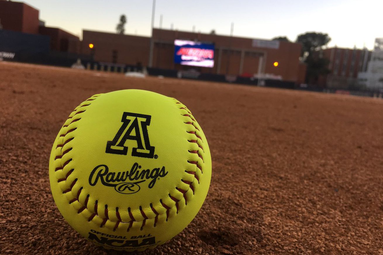 Photo of a yellow softball with the letter A and the word “Rawlings” on it lying on a field